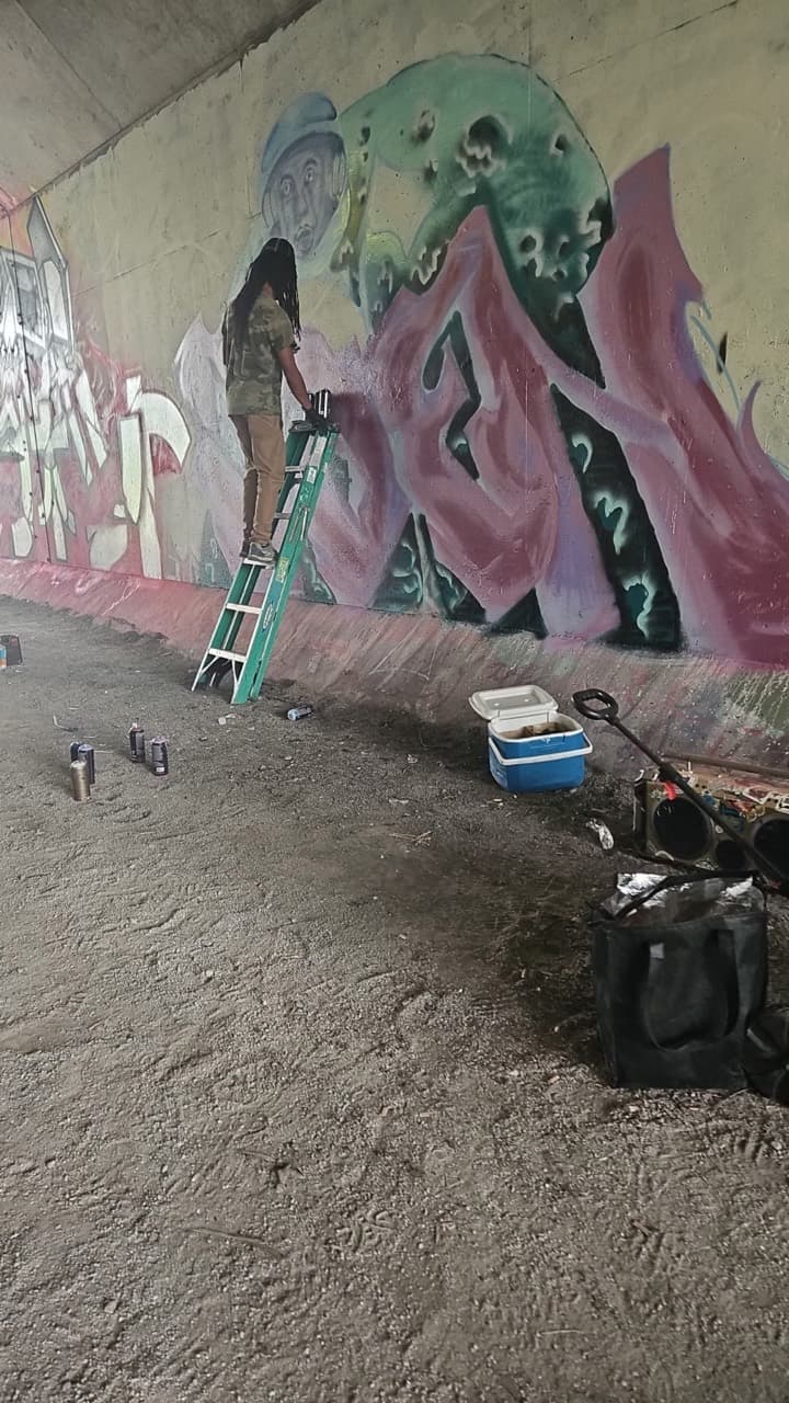 Quinton Trott painting a mural from a ladder during a community art event